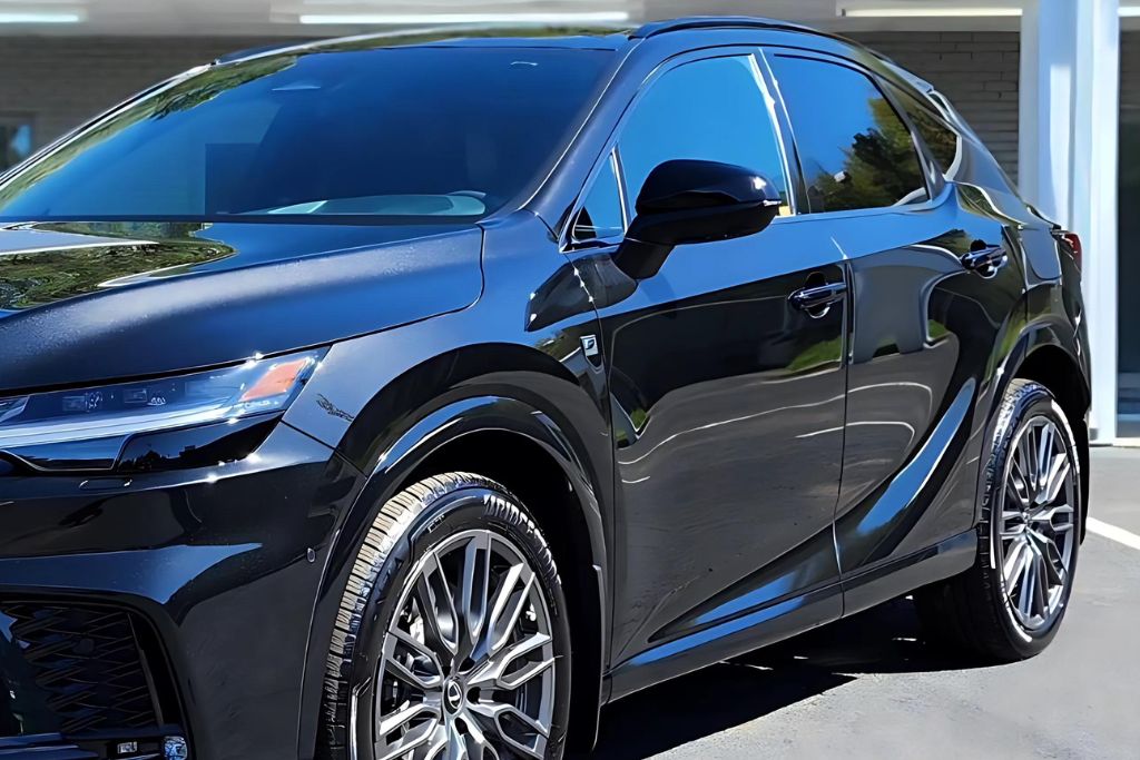 The image shows a sleek black SUV with glossy paint, reflecting its surroundings. The car is parked in an outdoor setting under a bright sky, emphasizing its polished finish and stylish design. The tires and wheels are prominently displayed, highlighting their clean, detailed look.