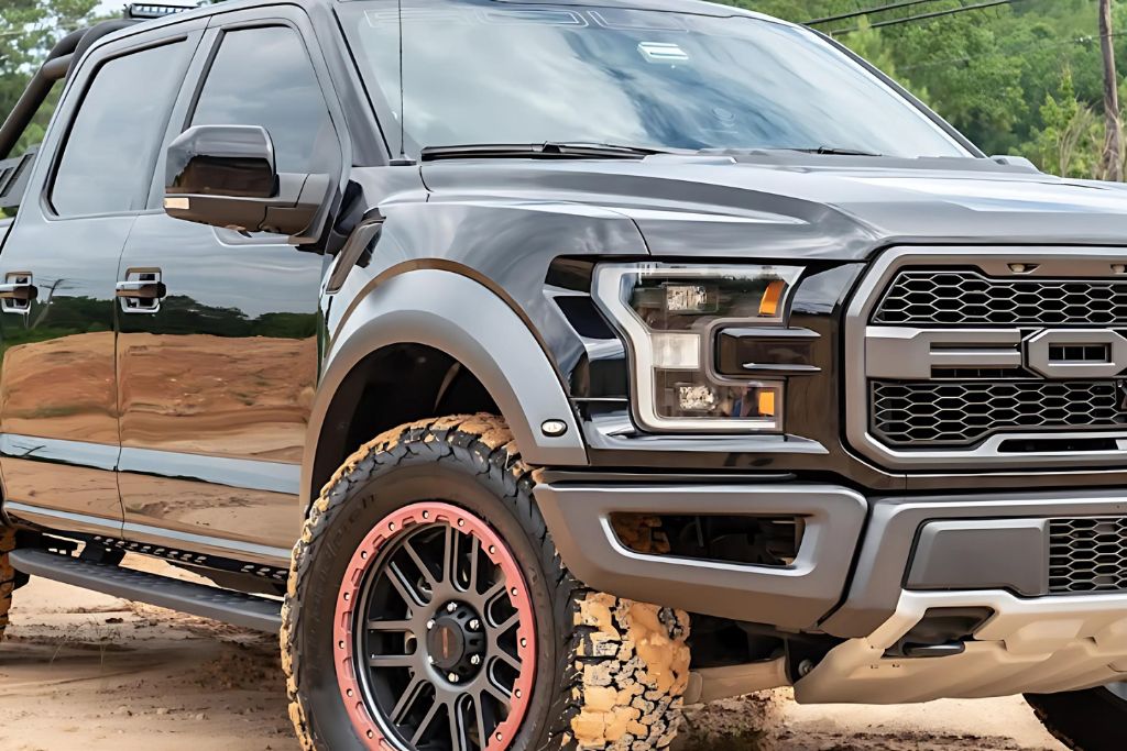 A shiny black truck with clean, polished paint driving through a muddy area, showcasing its well-maintained surface despite rough conditions.