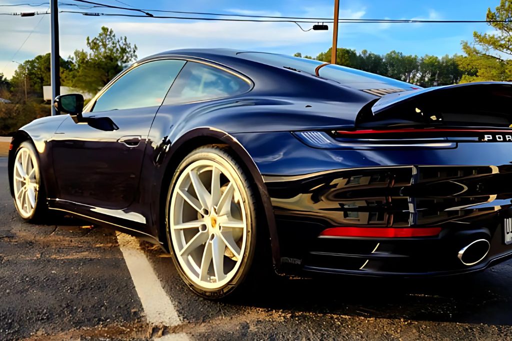 A sleek black Porsche sports car with tinted windows, parked outdoors under a clear sky. The vehicle’s reflective finish and pristine window tinting highlight the quality work by Slick Obsession.