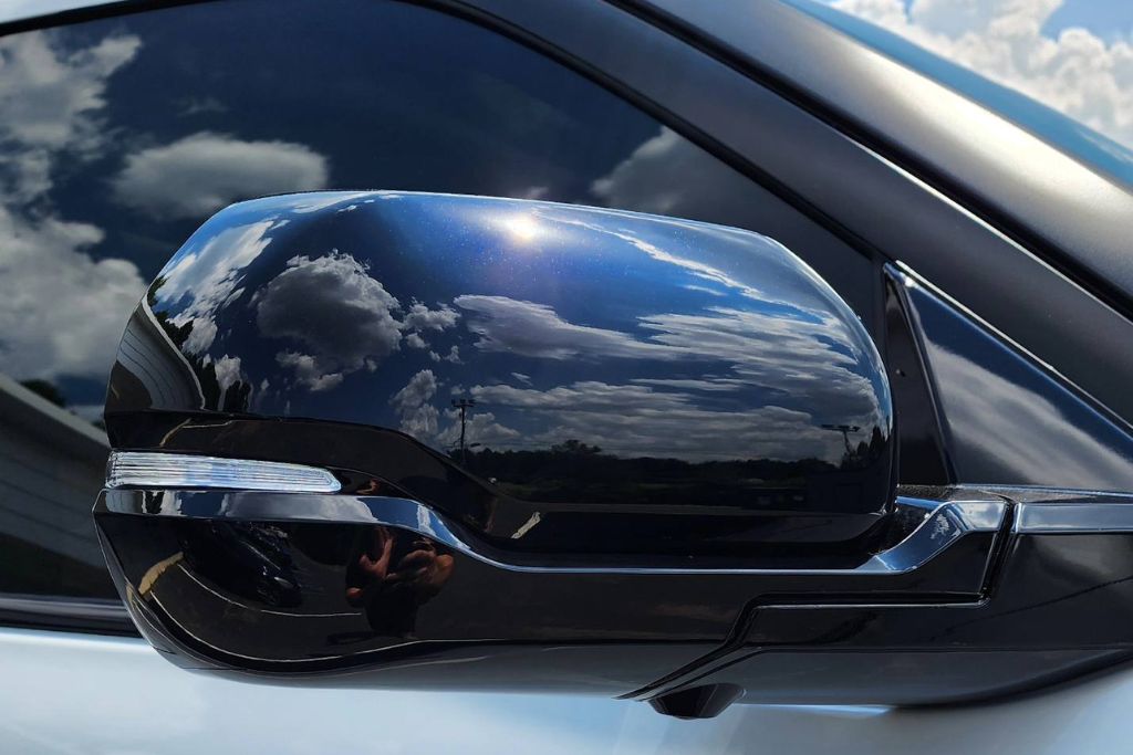 Close-up of a car's side mirror and window with high-quality tint, reflecting a vivid blue sky with clouds. The tint provides a sleek appearance while balancing privacy and visibility, ideal for day and night driving.