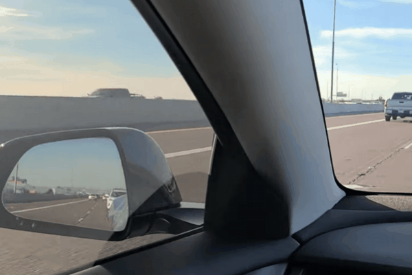 View from inside a car showcasing a side mirror and window with ceramic tint, overlooking a highway under a clear blue sky. The tinted glass highlights premium features like UV protection and heat rejection while maintaining visibility.