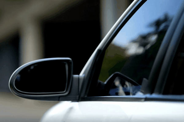 A close-up of a car's side mirror and window with privacy tint, reflecting a blurred outdoor background. The sleek, tinted glass emphasizes both style and functionality, offering increased privacy and reduced glare.